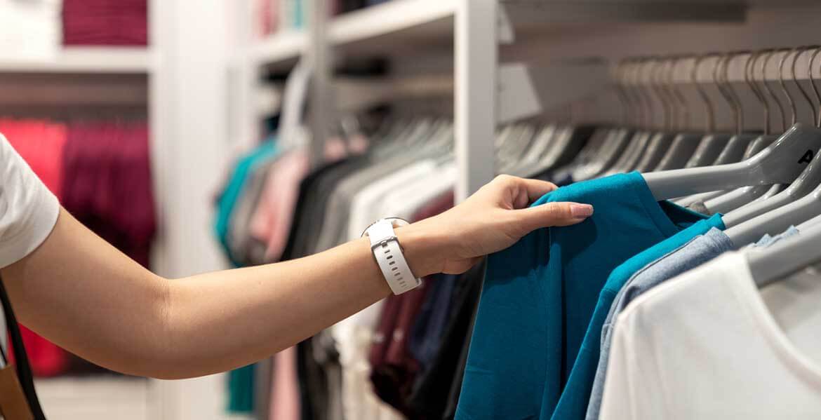 Person lifting a t-shirt from a clothing rail in a fast fashion store