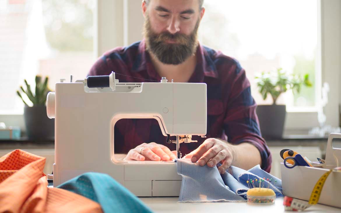 Photo of a man using a sewing machine to sew blue fabric