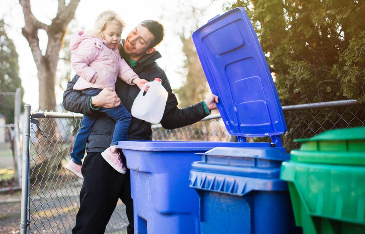 A father and daughter put milk bottle into recycling bin