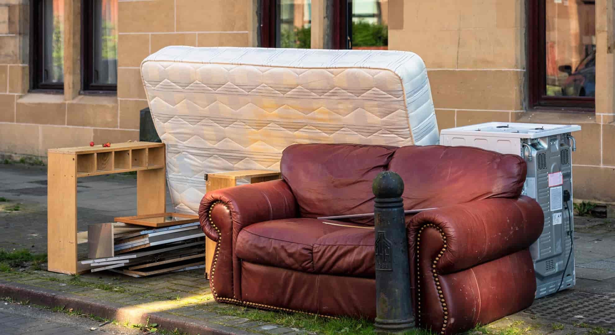 a group of household items, including a sofa, mattress and cooker, left on the kerbside