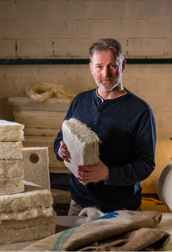 Man Standing holding a bundle of Sisal material in front of sacks and stacks of Sisal blocks