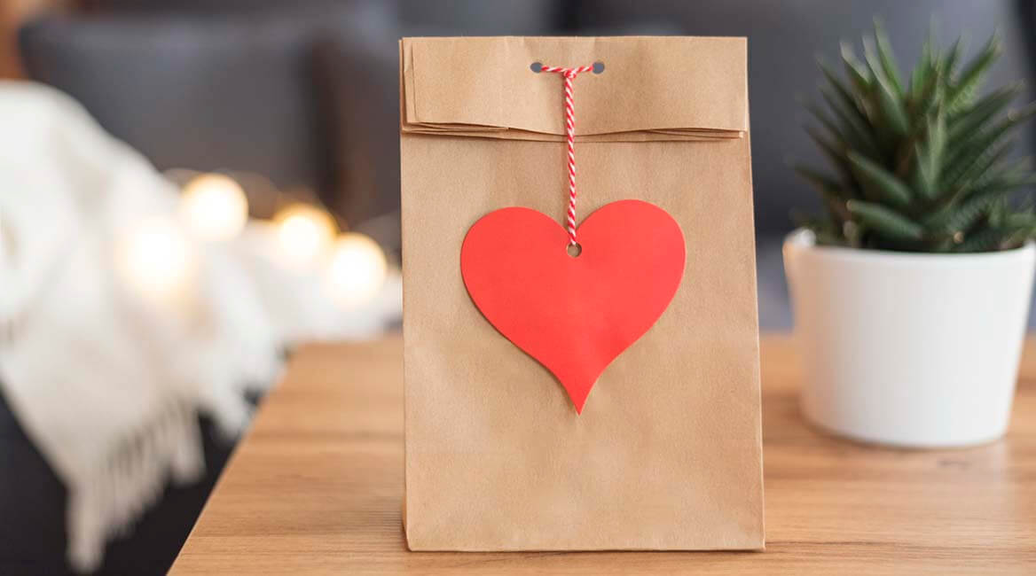 Valentine's gift in a brown paper bag with a red love heart on a coffee table beside a potted plant