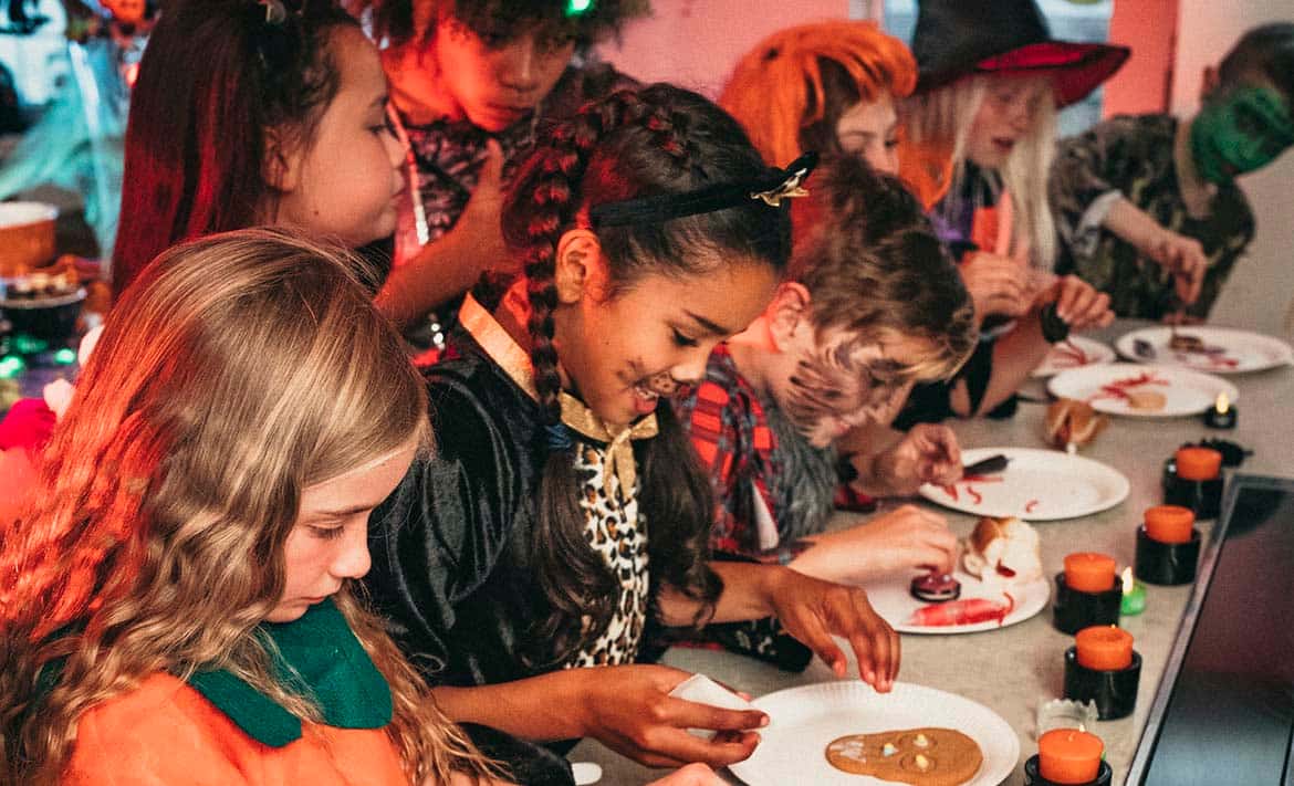 Photo of a group of children dressed in Halloween costumes decorating Halloween cookies