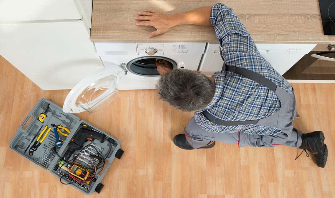 Photo of a repairman repairing a washing machine with a tool box on the floor