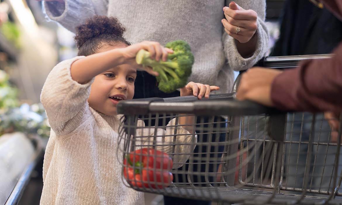 Child putting broccoli in shopping basket