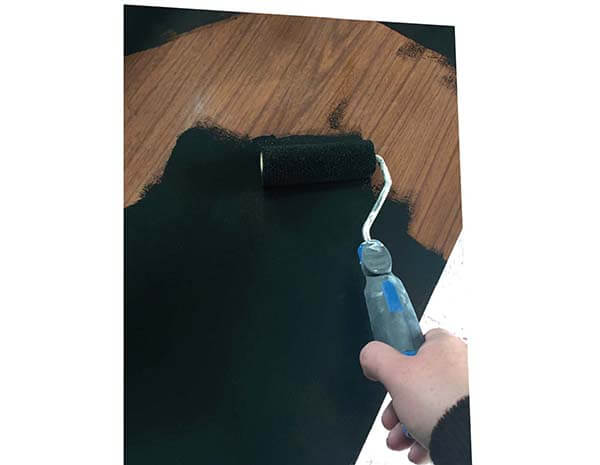 Paint roller applying black paint to wooden surface