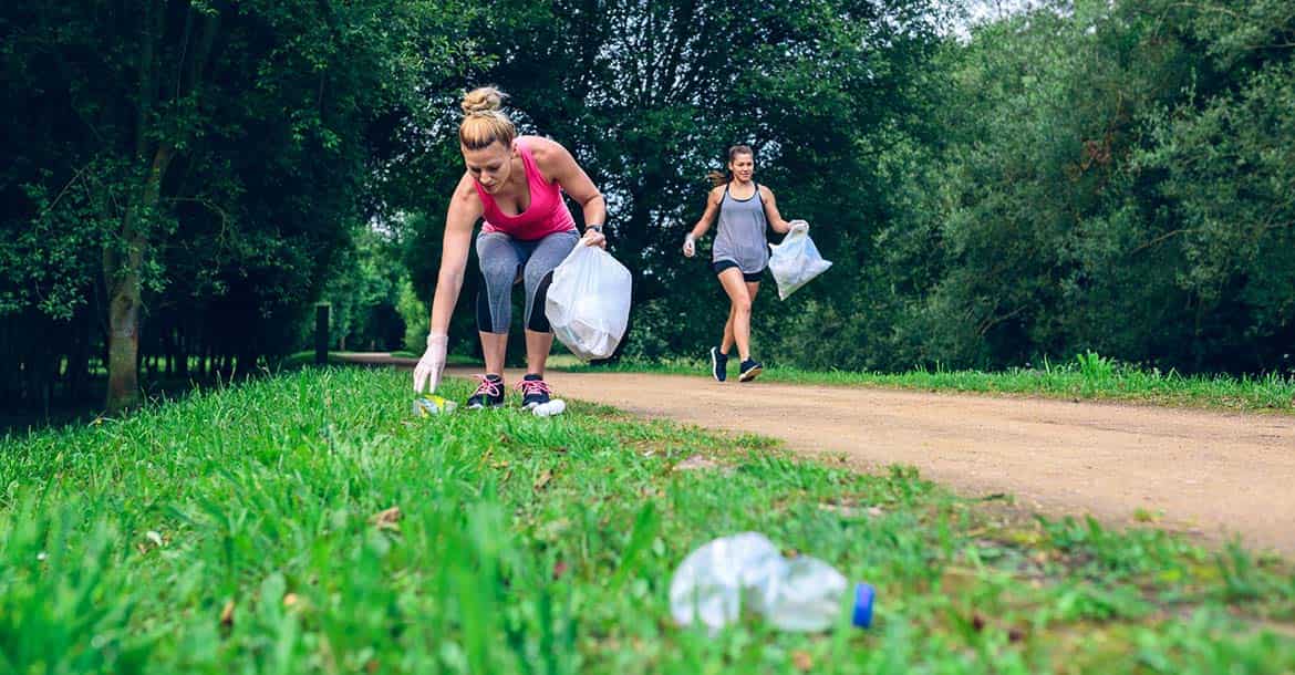 Two women jogging with bags, picking up rubbish as they jog