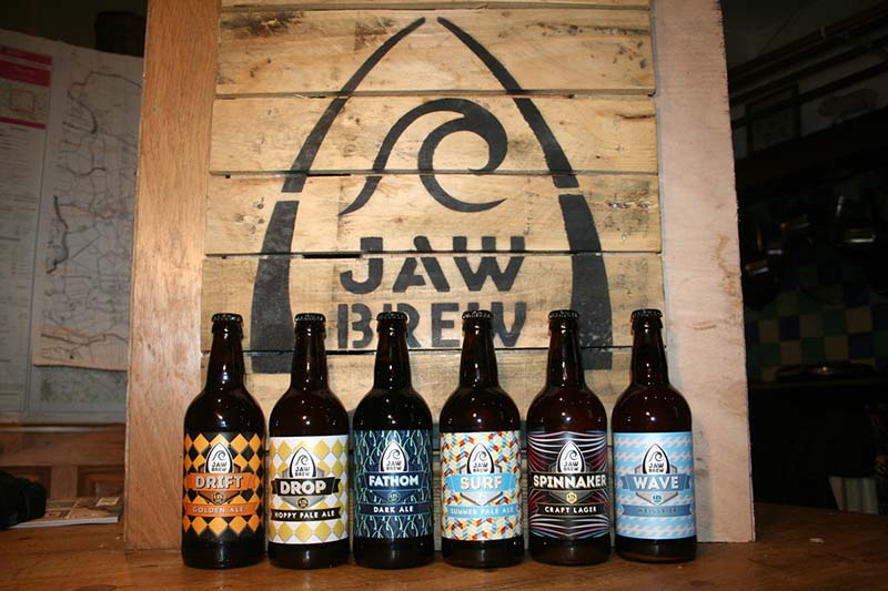 Photo of a row of six beer bottles with the Jaw Brew logo in background