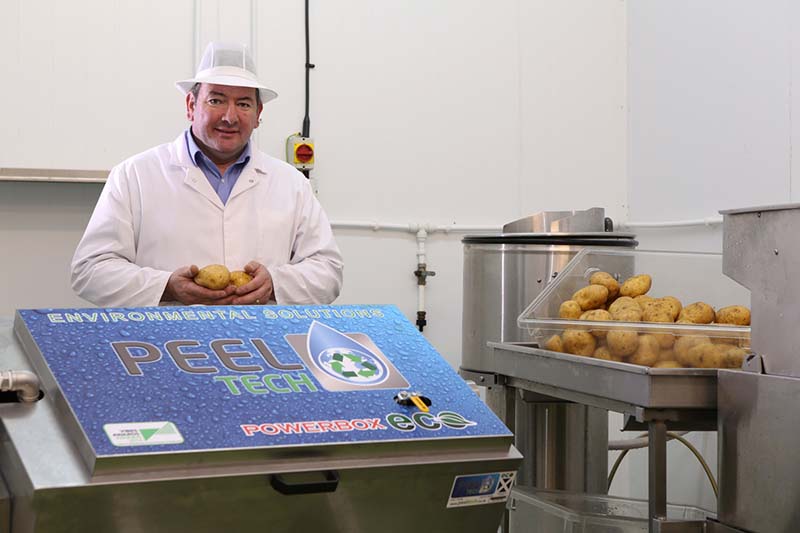 Photo of a man wearing a white coat and hat beside a container of potatoes