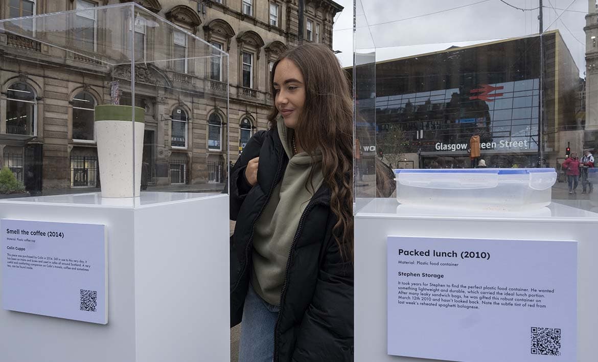A person looking at a reusable coffee cup on an exhibition plinth in Glasgow