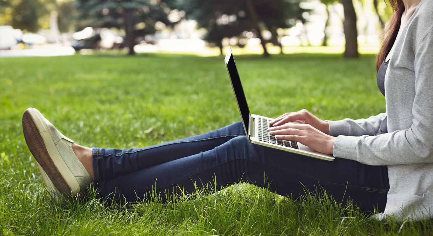A person sitting outside on grass working on a laptop computer
