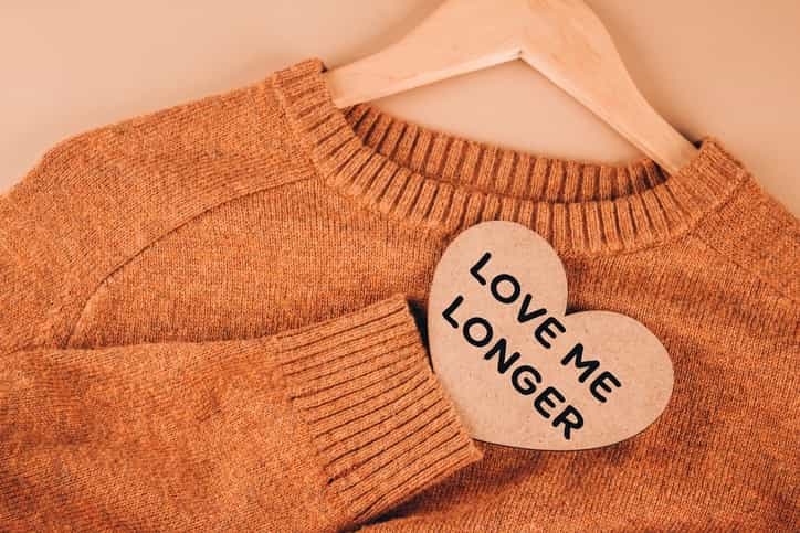 An orange jumper on a hanger, along with a wooden heart that says "love me longer"