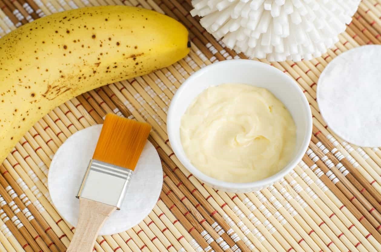 DIY banana mask in a bowl, with banana and application brush in the background