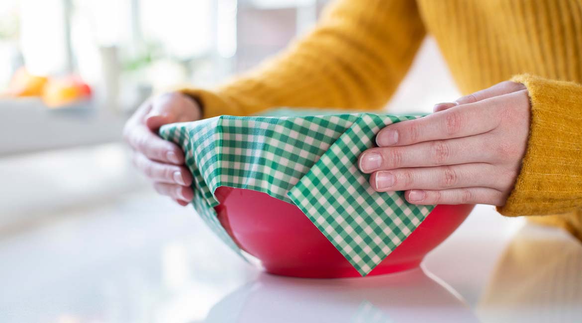Photo of a person covering a bowl with a green reusable wax wrap to avoid single-use cling film
