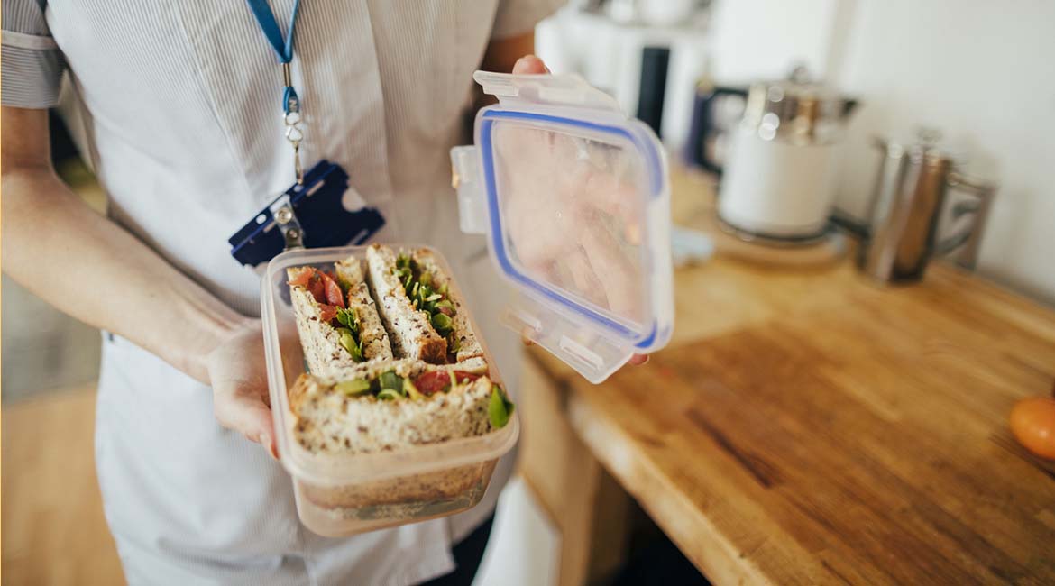 Photo of a person wearing a nurses uniform holding a sandwich in a resuable lunch box to avoid single-use cling film