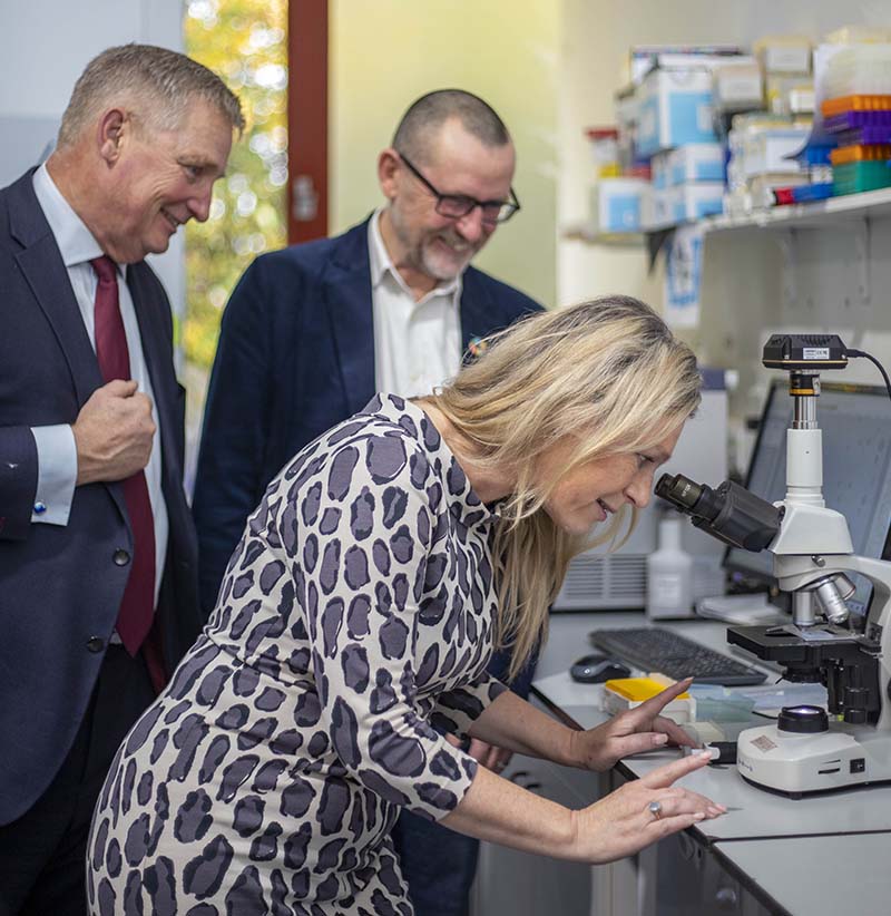 Photo of Zero Waste Scotland Chief Executive Iain Gulland, Chair, Dominic Fry, and Cabinet Secretary for Net Zero and Energy, Gillian Martin MSP looking into a microscope at pioneering biotech start-up, MiAlgae, in Edinburgh